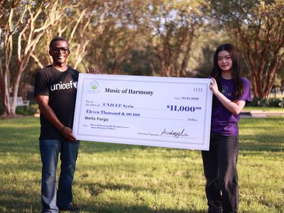 Music of Harmony leaders stand with donation check.