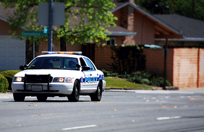 White police patrol car with roof light bar parked on a residential street.
