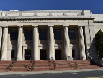 The Contra Costa County Courthouse, a large stone building with tall columns and a wide staircase leading to its entrance, under a clear blue sky.