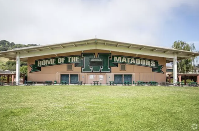 Exterior of a covered outdoor pavilion at Miramonte High School with a large "Home of the Matadors" sign featuring the school's green "M" logo, overlooking a grassy field.