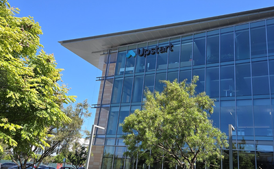 Exterior view of Upstart's glass headquarters building in Burlingame, with the company's logo mounted on the facade above ground-level windows, surrounded by trees.