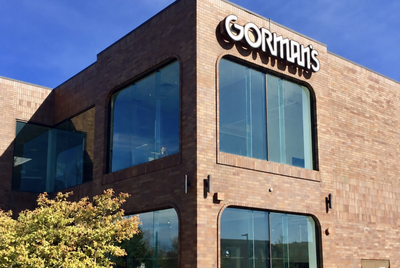 Exterior of a Gorman's Home Furnishings & Interior Design showroom, a two-story brick building with large arched windows and the Gorman's logo above the entrance, set against a blue sky.