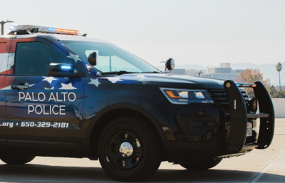 A Palo Alto Police SUV with an American flag design and light bar, parked in a lot with a hazy skyline in the background.