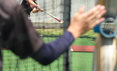 A young baseball player swings a bat inside a batting cage on an artificial turf field.