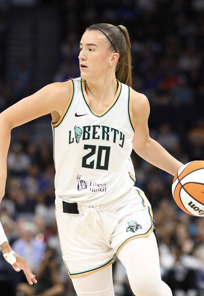 WNBA guard Sabrina Ionescu, wearing a white New York Liberty jersey number 20, dribbles a basketball during a game, with a blurred arena crowd in the background.
