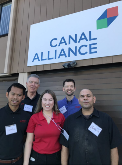 Five people stand outside Canal Alliance's San Rafael office beneath the organization's sign, several wearing name tags and two in Toyota Marin polo shirts.