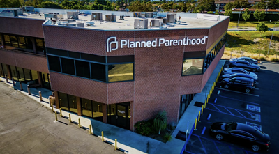 Exterior of a brick Planned Parenthood clinic building with a parking lot, aerial view.